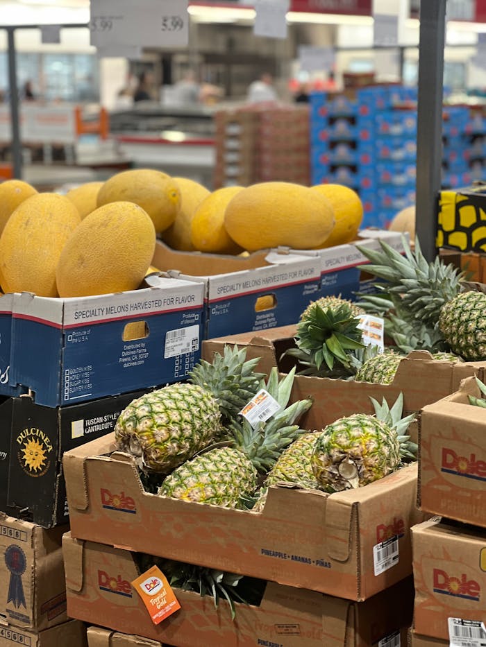 Boxes of pineapples and melons in a grocery store aisle.
